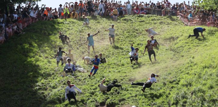 Los participantes de la segunda carrera masculina ruedan cuesta abajo persiguiendo un queso Double Gloucester redondo durante la competición anual de rodar quesos de Cooper's Hill, cerca del pueblo de Brockworth, Gloucester, en el oeste de Inglaterra. La competición anual de rodar quesos de Cooper's Hill consiste en que los participantes persigan un queso Double Gloucester de ocho libras (3,63 kg) cuesta abajo por una pendiente pronunciada.