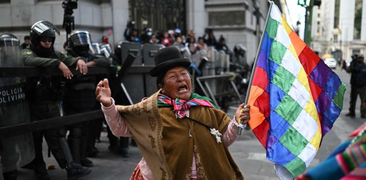 Una mujer indígena que sostiene una bandera wiphala hace un gesto frente a la policía antidisturbios durante una protesta contra el gobierno del presidente Rodrigo Paz en La Paz.
