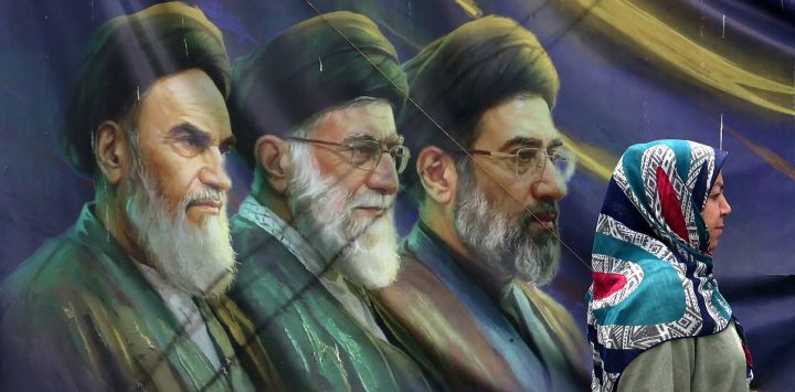 Una mujer iraní pasa junto a una pancarta con retratos del difunto fundador de la República Islámica, el ayatolá Ruhollah Khomeini (izquierda), el exlíder supremo ayatolá Ali Khamenei (centro), asesinado en febrero de 2026, y el actual líder supremo Mojtaba Khamenei (derecha), en Teherán, Irán.