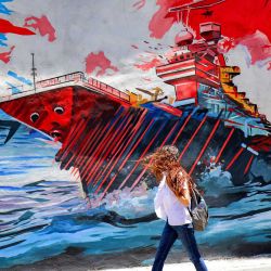 Una mujer pasa junto a un mural antiestadounidense y antiisraelí que representa misiles impactando un portaaviones en Teherán, Irán. | Foto:ATTA KENARE / AFP