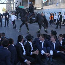 Policías israelíes montan guardia mientras judíos ultraortodoxos protestan contra el servicio militar obligatorio bloqueando la entrada a Jerusalén. Se oponen a una modificación de la ley sobre el servicio militar obligatorio, del que la comunidad ultraortodoxa ha estado tradicionalmente exenta. Según una disposición establecida cuando se fundó el país en 1948 —cuando la comunidad ultraortodoxa era pequeña—, los hombres que se dedican a tiempo completo al estudio de los textos sagrados judíos están exentos. | Foto:AHMAD GHARABLI / AFP