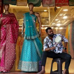 Un empleado se abanica mientras espera a los clientes frente a una tienda de ropa, en una calurosa tarde de verano en Varanasi, India. | Foto:NIHARIKA KULKARNI / AFP