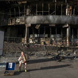 Un niño toca el acordeón frente a un centro comercial dañado por los ataques rusos en Kiev, en medio de la invasión rusa de Ucrania. | Foto:Vladyslav Musiienko / AFP