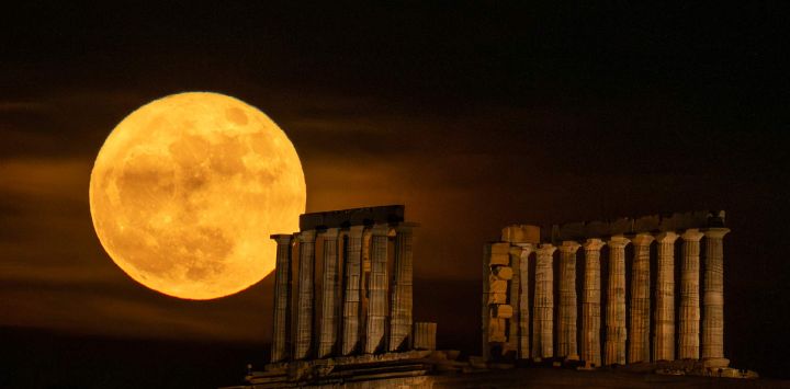 La luna llena se eleva tras el antiguo templo griego de Poseidón en el cabo Sunión, a unos 60 kilómetros al sur de Atenas, Grecia.