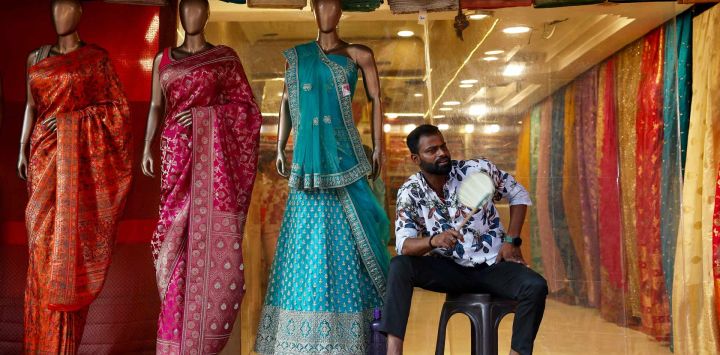 Un empleado se abanica mientras espera a los clientes frente a una tienda de ropa, en una calurosa tarde de verano en Varanasi, India.