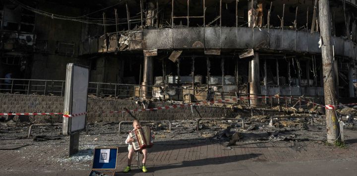 Un niño toca el acordeón frente a un centro comercial dañado por los ataques rusos en Kiev, en medio de la invasión rusa de Ucrania.