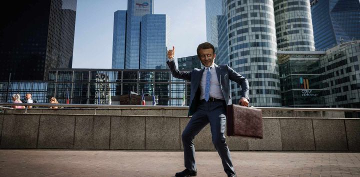Una persona con una máscara que representa al presidente francés Emmanuel Macron posa con la torre de la sede de TotalEnergies de fondo mientras participa en una protesta organizada por las asociaciones Attac, Avaaz, 350 y Action Justice Climat Paris, en el marco de la junta general anual de la compañía, para denunciar "el apoyo financiero y político que el grupo sigue recibiendo, a pesar de sus proyectos de combustibles fósiles en curso y sus impactos humanos, climáticos y ambientales", en la explanada del distrito comercial de La Défense en Puteaux.