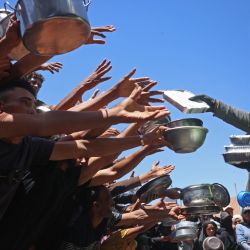 Palestinos desplazados se reunieron para recibir comidas calientes distribuidas por un comedor social en Khan Yunis, al sur de la Franja de Gaza. Esta distribución de alimentos se produjo en medio de la continua escasez de suministros alimenticios causada por los ataques israelíes y las restricciones a la entrada de ayuda humanitaria en la Franja de Gaza. | Foto:Bashar Taleb / AFP