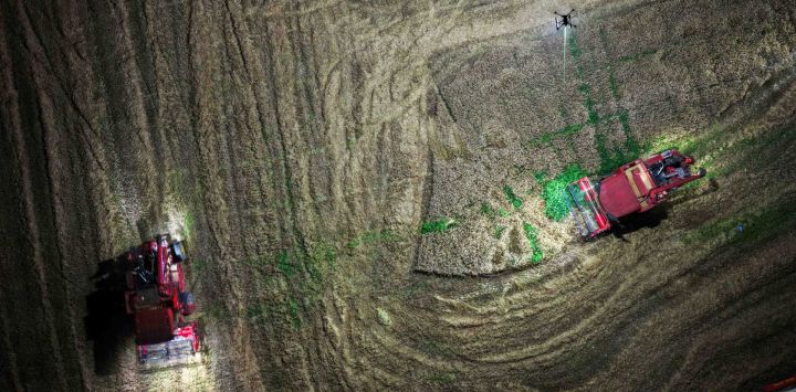 Vista aérea tomada con un dron de máquinas agrícolas cargando trigo cosechado en un camión en un campo iluminado por un dron de iluminación de alta potencia conectado por cable, en la ciudad de Hefei, en la provincia de Anhui, en el este de China.
