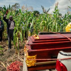 Un pastor local levanta la mano en oración mientras miembros de un equipo de la Cruz Roja Congoleña, con equipo de protección personal, colocan el ataúd de una mujer presuntamente fallecida por la enfermedad del virus del Ébola en una camioneta, antes de su entierro seguro en su casa en Bunia. La UE anunció el envío de 100 toneladas de ayuda humanitaria a una zona de difícil acceso en el este de la República Democrática del Congo, afectada por un brote de Ébola. | Foto:Jospin Mwisha / AFP
