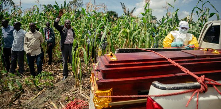 Un pastor local levanta la mano en oración mientras miembros de un equipo de la Cruz Roja Congoleña, con equipo de protección personal, colocan el ataúd de una mujer presuntamente fallecida por la enfermedad del virus del Ébola en una camioneta, antes de su entierro seguro en su casa en Bunia. La UE anunció el envío de 100 toneladas de ayuda humanitaria a una zona de difícil acceso en el este de la República Democrática del Congo, afectada por un brote de Ébola.