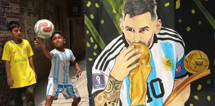 Imagen de niños aficionados jugando fútbol alrededor de una calle decorada con exhibiciones temáticas futbolísticas, en la zona de Tikatuli de Dhaka, Bangladesh. El "Callejón de la FIFA" del barrio se ha convertido en un lugar de encuentro para los aficionados al fútbol previo a la Copa Mundial de la FIFA 2026.