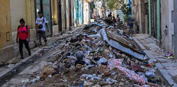 Varias personas caminan junto a montones de basura en una calle de La Habana, Cuba.