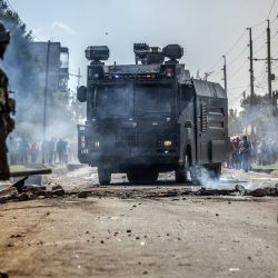 Agentes de la policía keniana vigilan una carretera mientras un vehículo policial con cañón de agua retira barricadas durante los enfrentamientos con manifestantes en una protesta contra un controvertido centro de cuarentena para el ébola construido por Estados Unidos, en la base aérea de Laikipia, en Nanyuki. Varios kenianos fueron arrestados ese mismo día en las últimas protestas contra la construcción de un centro de cuarentena para ciudadanos estadounidenses en una ciudad turística. | Foto:LUIS TATO / AFP