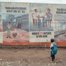 Un niño que regresa de la escuela se detiene a observar las ilustraciones sobre el ébola expuestas en los letreros del Centro de Tratamiento del Ébola (CTE) en Munigi. El único aeropuerto que da acceso a las organizaciones humanitarias al epicentro del brote de ébola en la República Democrática del Congo reabrió sus puertas tras la disminución del número de casos sospechosos notificados. | Foto:Jospin Mwisha / AFP