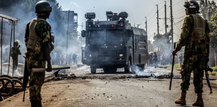 Agentes de la policía keniana vigilan una carretera mientras un vehículo policial con cañón de agua retira barricadas durante los enfrentamientos con manifestantes en una protesta contra un controvertido centro de cuarentena para el ébola construido por Estados Unidos, en la base aérea de Laikipia, en Nanyuki. Varios kenianos fueron arrestados ese mismo día en las últimas protestas contra la construcción de un centro de cuarentena para ciudadanos estadounidenses en una ciudad turística.