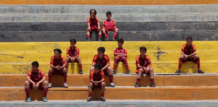 Jóvenes iraníes se sientan en las tribunas durante una sesión de entrenamiento en un centro de fútbol en Teherán.