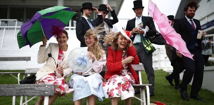Los asistentes a las carreras luchan contra el viento antes del inicio del segundo día del Festival de Carreras de Caballos de Epsom, en Surrey, al sur de Inglaterra.