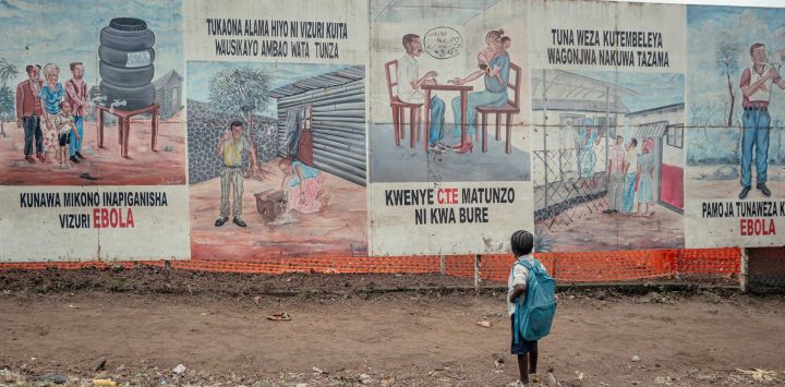Un niño que regresa de la escuela se detiene a observar las ilustraciones sobre el ébola expuestas en los letreros del Centro de Tratamiento del Ébola (CTE) en Munigi. El único aeropuerto que da acceso a las organizaciones humanitarias al epicentro del brote de ébola en la República Democrática del Congo reabrió sus puertas tras la disminución del número de casos sospechosos notificados.