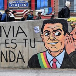 Jóvenes caminan junto a un muro con murales antigubernamentales durante un bloqueo vial en la zona de Río Seco, El Alto, Bolivia. Bolivia ha enfrentado días de protestas y bloqueos viales en medio de crecientes tensiones políticas y escasez de suministros que afectan a diferentes regiones del país. | Foto:MARVIN RECINOS / AFP