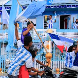 Muhammad Yusuf (atrás, centro), aficionado argentino y pescador, sostiene una réplica del trofeo de la Copa Mundial mientras los aficionados al fútbol pasan frente a su casa, pintada con los colores de la selección argentina, en una caravana que daba la bienvenida al Mundial de Fútbol de la FIFA 2026 en Polewali Mandar, en el oeste de Sulawesi, Indonesia. | Foto:Muhammad Salim / AFP