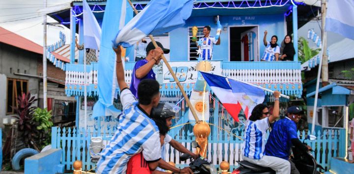 Muhammad Yusuf (atrás, centro), aficionado argentino y pescador, sostiene una réplica del trofeo de la Copa Mundial mientras los aficionados al fútbol pasan frente a su casa, pintada con los colores de la selección argentina, en una caravana que daba la bienvenida al Mundial de Fútbol de la FIFA 2026 en Polewali Mandar, en el oeste de Sulawesi, Indonesia.