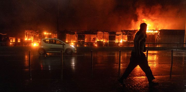 Un residente camina frente a un mercado en llamas tras un ataque con misiles rusos en Kiev, en medio de la invasión rusa de Ucrania. Rusia lanzó una andanada de misiles contra varias ciudades importantes de Ucrania, incendiando la histórica Catedral de la Dormición de Kiev y causando nueve muertos, mientras que los ataques ucranianos cobraron tres vidas al sur de Moscú.