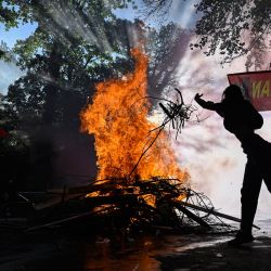 Un manifestante arroja ramas al fuego de un contenedor de basura en llamas durante una concentración de la coalición "No al G7", integrada por más de 60 asociaciones, sindicatos y grupos de izquierda "contra el fascismo y el imperialismo", en Ginebra, Suiza. | Foto:GABRIEL MONNET / AFP