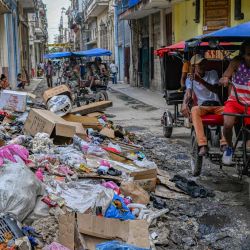 Una persona con una camiseta con la bandera de Estados Unidos pasa en triciclo junto a un montón de basura en una calle de La Habana, Cuba. | Foto:YAMIL LAGE / AFP