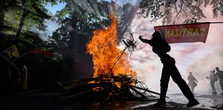 Un manifestante arroja ramas al fuego de un contenedor de basura en llamas durante una concentración de la coalición "No al G7", integrada por más de 60 asociaciones, sindicatos y grupos de izquierda "contra el fascismo y el imperialismo", en Ginebra, Suiza.