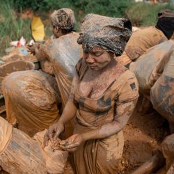 Mujeres mineras, cubiertas con bolsas de plástico sobre su ropa, conocidas localmente como "decalots" para protegerse del barro y la suciedad, limpian rocas en el agua en busca de partículas de oro en un yacimiento minero artesanal en Mongbwalu, provincia de Ituri. El último brote de ébola en la República Democrática del Congo, declarado el 15 de mayo de 2026, ha afectado principalmente a la remota provincia nororiental de Ituri, azotada por el conflicto. Las autoridades sanitarias advierten que los movimientos de población vinculados a la minería artesanal, el desplazamiento y la inseguridad están dificultando los esfuerzos de contención en una región donde no existe una vacuna aprobada para esta cepa de ébola. | Foto:Jospin Mwisha / AFP