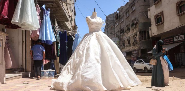 Una mujer palestina pasa junto a un taller de costura donde se confeccionan vestidos, incluyendo vestidos de noche y de novia, a pesar de los escasos recursos, y donde se reciclan vestidos viejos en la ciudad de Khan Yunis, en el sur de la Franja de Gaza.