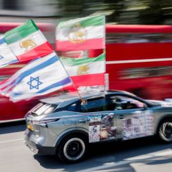 Un coche con banderas estadounidenses, israelíes y otras anteriores a la revolución de 1979 ondean al pasar junto a un grupo de manifestantes antirrégimen iraní reunidos frente al Parlamento en el centro de Londres, Inglaterra. | Foto:Brook Mitchell / AFP
