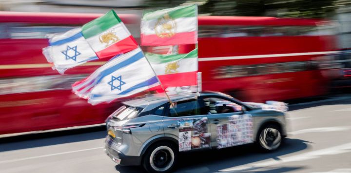 Un coche con banderas estadounidenses, israelíes y otras anteriores a la revolución de 1979 ondean al pasar junto a un grupo de manifestantes antirrégimen iraní reunidos frente al Parlamento en el centro de Londres, Inglaterra.