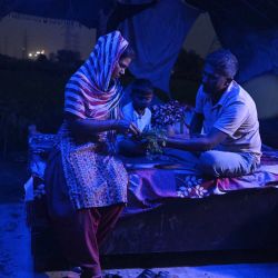 Esta fotografía muestra a Debvati (izquierda) conversando con su esposo, el agricultor Bhole Shankar, dentro de su humilde vivienda al anochecer, en las llanuras aluviales del río Yamuna, en Nueva Delhi. En las exuberantes riberas verdes de las llanuras aluviales del río Yamuna, en Nueva Delhi, los veranos abrasadores se han vuelto cada vez más difíciles de soportar, lo que exige adaptaciones y obliga a la vida a transcurrir durante las horas de oscuridad antes de que el sol se vuelva implacable. La capital de la India alcanzó los 46,5 °C este verano, todavía por debajo del récord de 49,9 °C registrado en 2024. | Foto:ARUN SANKAR / AFP