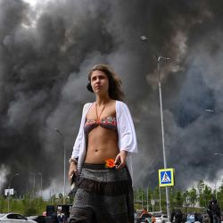 Una mujer camina frente a un centro comercial mientras una columna de humo negro se eleva desde la refinería de petróleo de Gazprom Neft, la petrolera rusa ubicada en las afueras del sureste de Moscú. Moscú se defendía de un ataque con drones a gran escala proveniente de Ucrania, y varios drones lograron alcanzar una refinería de petróleo, según declaró el alcalde de la ciudad, Serguéi Sobianin. | Foto:AFP