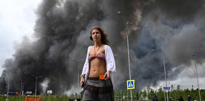 Una mujer camina frente a un centro comercial mientras una columna de humo negro se eleva desde la refinería de petróleo de Gazprom Neft, la petrolera rusa ubicada en las afueras del sureste de Moscú. Moscú se defendía de un ataque con drones a gran escala proveniente de Ucrania, y varios drones lograron alcanzar una refinería de petróleo, según declaró el alcalde de la ciudad, Serguéi Sobianin.
