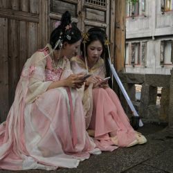 Visitantes ataviados con trajes tradicionales consultan sus teléfonos en la pintoresca ciudad de Wuzhen, en la provincia oriental china de Zhejiang. | Foto:Hector Retamal / AFP