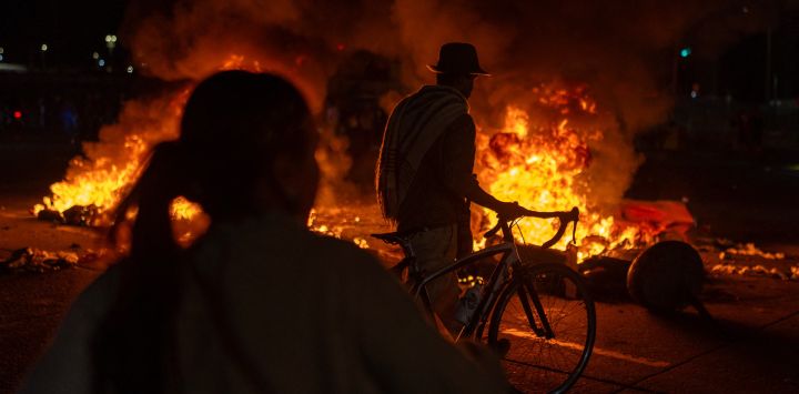 Un hombre camina con su bicicleta mientras manifestantes se encuentran frente a barricadas en llamas durante los enfrentamientos por los resultados preliminares de la segunda vuelta de las elecciones presidenciales en Bogotá, Colombia.
