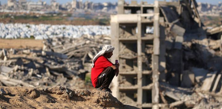 Un hombre se sienta en la cima de una colina cerca de edificios destruidos y gravemente dañados en el campamento de refugiados palestinos de Nuseirat, en el centro de la Franja de Gaza.