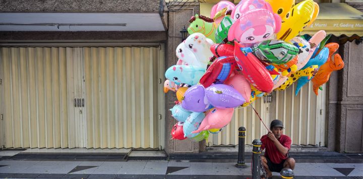 Un vendedor de globos se sienta frente a tiendas cerradas durante el Festival de la Moda de Surabaya en una calle de Surabaya, Indonesia.