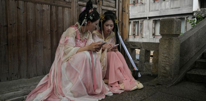 Visitantes ataviados con trajes tradicionales consultan sus teléfonos en la pintoresca ciudad de Wuzhen, en la provincia oriental china de Zhejiang.