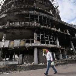 Un hombre lleva flores mientras camina junto a un centro comercial previamente destruido durante ataques con drones y misiles rusos, en Kiev, en medio de la invasión rusa de Ucrania. | Foto:SERGEI SUPINSKY / AFP