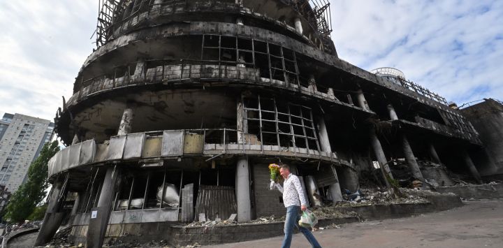 Un hombre lleva flores mientras camina junto a un centro comercial previamente destruido durante ataques con drones y misiles rusos, en Kiev, en medio de la invasión rusa de Ucrania.