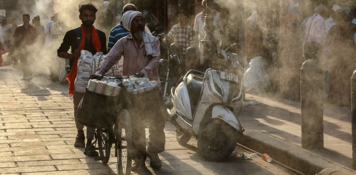 Varias personas caminan bajo los aspersores de agua instalados a lo largo de una calle en un caluroso día de verano en Varanasi, India.