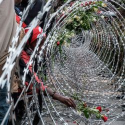 Agentes de la policía keniana observan cómo activistas colocan flores en la barrera de alambre de púas instalada para impedirles el acceso al recinto del Parlamento durante las manifestaciones que conmemoran el segundo aniversario de las mortales protestas juveniles contra la Ley de Finanzas de junio de 2024, en las que los manifestantes irrumpieron en el Parlamento, en Nairobi. | Foto:Kabir Dhanji / AFP