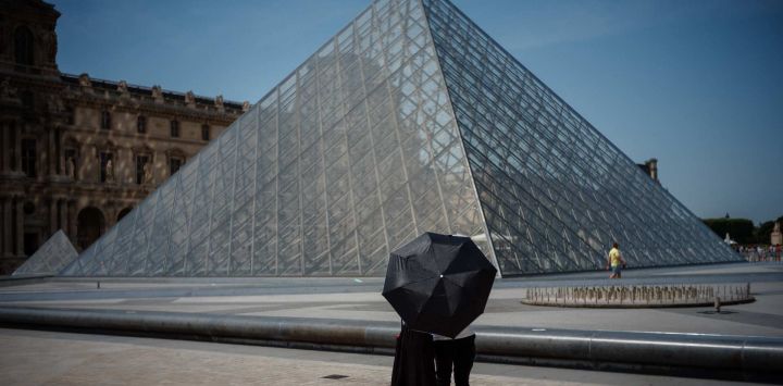 Una pareja se protege del sol bajo una sombrilla frente a la Pirámide del Louvre, diseñada por el arquitecto chino-estadounidense Ieoh Ming Pei, en París, durante una ola de calor en Francia.