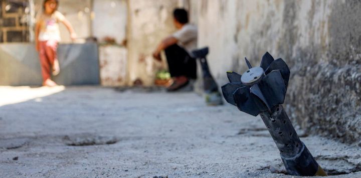 Un hombre conversa con un niño sentado cerca de un proyectil de artillería sin explotar que cayó durante el bombardeo israelí nocturno que impactó la aldea de Abidin, en la provincia de Daraa, al suroeste de Siria, cerca de los Altos del Golán. El Ministerio de Asuntos Exteriores de Siria condenó las incursiones y los bombardeos israelíes en el sur del país, un día después de que una escalada de violencia en la aldea, en la provincia de Daraa, obligara a sus residentes a huir temporalmente, según informaron funcionarios locales.