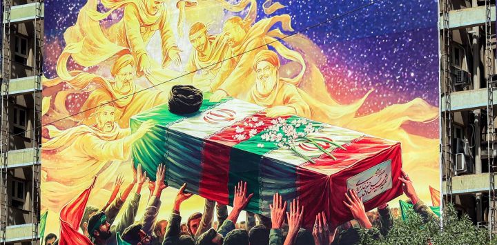 Un mural expuesto en la fachada de un edificio representa a figuras fallecidas alineadas con el gobierno iraní, como el difunto presidente Ebrahim Raisi, el difunto comandante de la Guardia Revolucionaria Islámica Qasem Soleimani, el difunto líder libanés de Hezbolá Hassan Nasrallah y otros, todos portando el ataúd cubierto con la bandera del difunto líder supremo de Irán, Ali Khamenei, quien murió en un ataque el primer día de la guerra entre Estados Unidos e Israel contra Irán, en la plaza Vanak de Teherán.