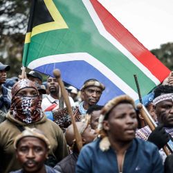 Miembros del regimiento zulú conocido como «Amabutho» portan una bandera sudafricana mientras marchan durante una manifestación del movimiento «Marcha y Marcha», que conmemora la fecha límite no oficial fijada por grupos ciudadanos para que los extranjeros indocumentados abandonen Sudáfrica, en Durban. | Foto:MARCO LONGARI / AFP